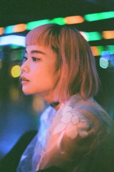 a young woman standing in front of brightly colored lights with her head turned to the side