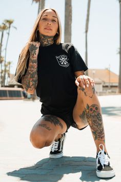 a woman sitting on the ground with tattoos on her arms and legs, wearing black sneakers