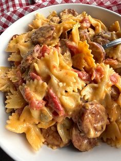 a white bowl filled with pasta and meat covered in sauce on top of a red checkered table cloth