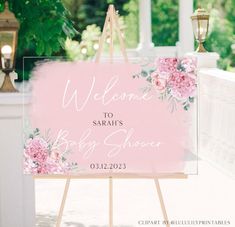 a welcome sign for a baby shower with pink flowers and greenery in the background