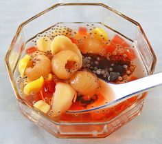 a glass bowl filled with fruit on top of a white table next to a spoon