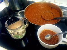 there is a pot and two cups on the stove with sauce in it, next to an empty mug