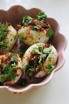 some food is in a pink bowl on a white table top and there are herbs sprinkled all over it