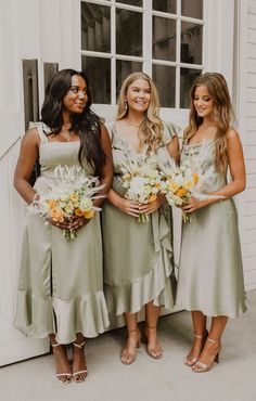 three bridesmaids in sage green dresses posing for the camera with their bouquets