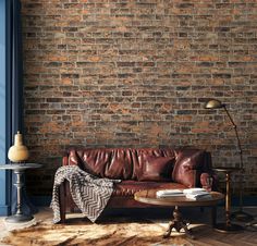 a brown leather couch sitting in front of a brick wall next to a wooden table