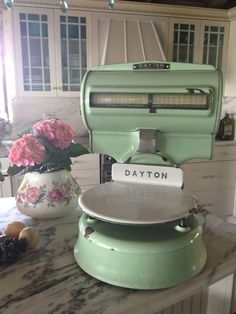 a green stove top oven sitting on top of a counter next to flowers and fruit