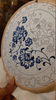 a hand embroidered blue and white floral design on a wooden hoop with a person holding it