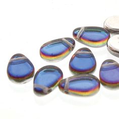 several blue and purple glass beads are on a white surface next to two silver buttons