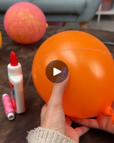 an orange ballon being held by someone's hand with markers and glue on the table