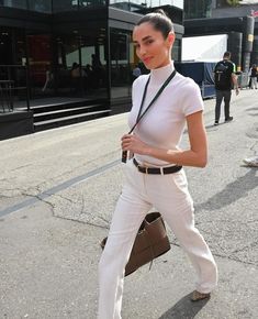 a woman is walking down the street with her hand in her pocket and wearing white pants