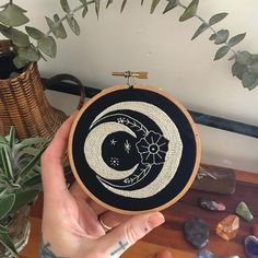 a person holding up a black and white embroidery hoop with a crescent moon on it