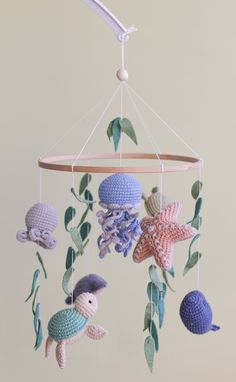 a crocheted sea animal mobile hanging from a ceiling fixture with leaves and shells