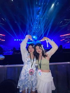 two young women standing next to each other in front of a stage with blue lights