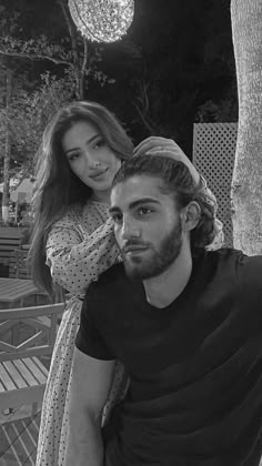 a man sitting next to a woman on top of a wooden bench in front of a tree