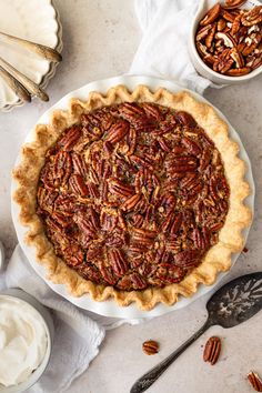 a pecan pie on a white plate next to other pecans and whipped cream