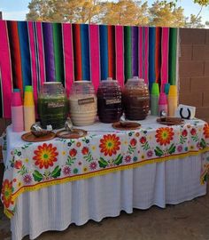 a table topped with jars filled with liquid next to a colorful wall covered in ribbons