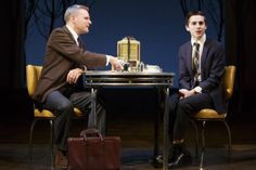 two men sitting at a table in front of a chess board on top of chairs