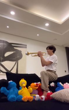 a young man sitting on top of a couch holding a trumpet next to stuffed animals