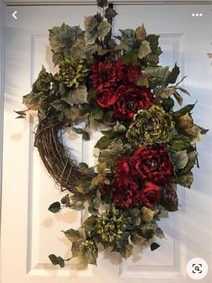 a wreath with red flowers and green leaves hangs on the front door's white door