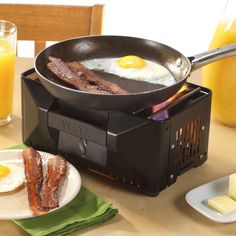 a frying pan with bacon and eggs on it sitting next to some glasses of orange juice