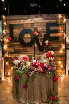 a table with flowers and lights on it in front of a wooden sign that says love