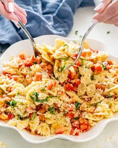 two hands holding spoons over a bowl of pasta with tomatoes and parmesan cheese