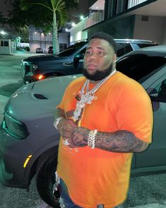 a man in an orange shirt is standing next to a car and holding a chain