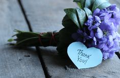 a bouquet of purple flowers with a heart shaped thank you note attached to the stems