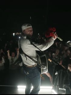 a man standing on top of a stage holding a red rose in his hand and singing into a microphone