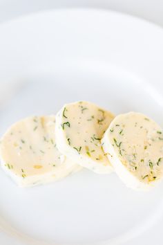 three pieces of food on a white plate with green sprigs and seasoning