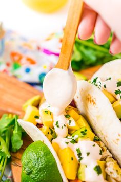 a person spooning dressing from a tortilla filled with corn and avocado