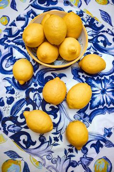 a bowl filled with lemons on top of a blue and white table cloth