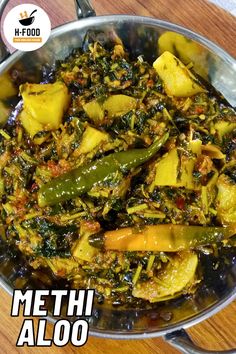 a metal pan filled with cooked vegetables on top of a wooden table and the words methi aloo above it