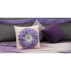 a bed with purple and white pillows and a large flower on the pillow cover in front of it