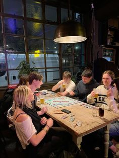 a group of people sitting around a wooden table in a restaurant eating pizza and drinking beer