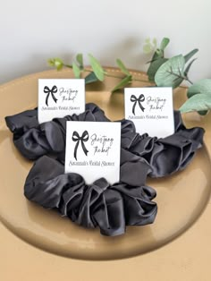 three black scrunffles with name tags on them sitting on a brown plate