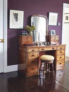 a wooden desk with a mirror and stool on it in front of a purple wall