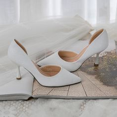 a pair of white high heeled shoes sitting on top of a table next to an open book