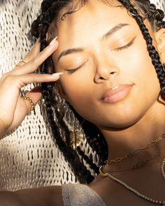 a woman with her eyes closed and hands on her head, wearing gold necklaces