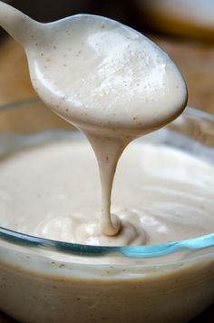 a spoon full of white sauce in a glass bowl