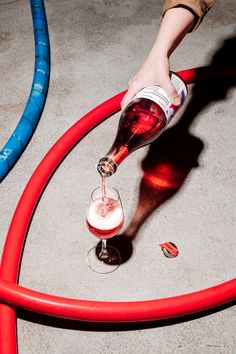 a person pouring wine into a glass on the floor next to hoses and bottles