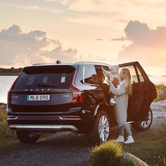 two people standing next to a black car with the door open and one person holding a white dog