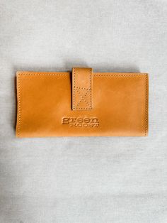 Introducing our custom line of leather handbags and accessories! Ethically made exclusively for Green Roost in Ethiopia and only available here! This is a limited edition collection, so snag yours before they're gone forever! This luxurious leather wallet will bring a timelessly classic look to your style. Crafted with quality Ethiopian leather & precision stitching, it strikes the perfect balance between elegance & durability. Its slim silhouette ensures convenience & its subtle embossed logo a Leather Travel Wallet In Cognac, Cognac Wallet With Leather Lining For Daily Use, Travel Wallet In Cognac With Leather Lining, Cognac Leather Wallet For Daily Use, Everyday Leather-lined Clutch Wallet, Everyday Leather Lined Clutch Wallet, Everyday Clutch Wallet With Leather Lining, Rectangular Cognac Wallet, Cognac Leather Wallets For Gift