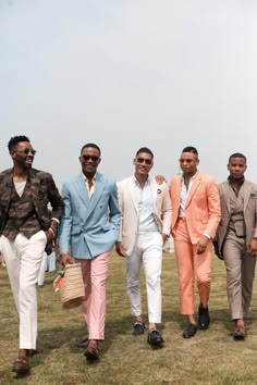 four men in suits are walking on the grass with one man wearing sunglasses and holding a straw hat