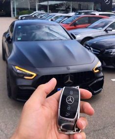 a hand holding a car key in front of a mercedes dealership with other cars