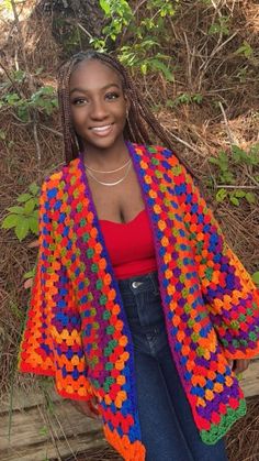 a woman wearing a colorful crochet shawl standing in front of some trees