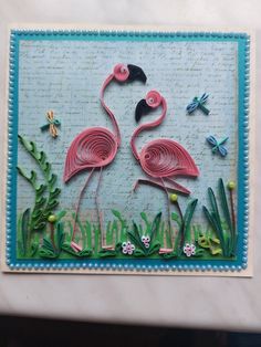 a card with two flamingos in the grass and dragonflies on it, all made out of paper