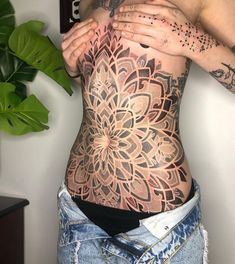 a woman with tattoos on her stomach holding onto the back of her body, while wearing ripped jeans