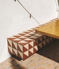 a yellow and brown bench sitting on top of a brick floor next to a white wall