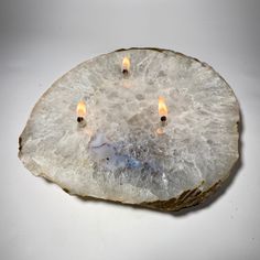 three lit candles are placed in the center of a large piece of rock that looks like it is floating on water